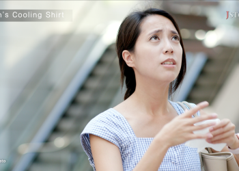 Close-up of a concerned-looking woman wiping sweat from her face in a warm outdoor setting.