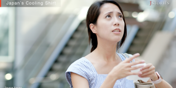 Close-up of a concerned-looking woman wiping sweat from her face in a warm outdoor setting.