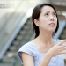 Close-up of a concerned-looking woman wiping sweat from her face in a warm outdoor setting.